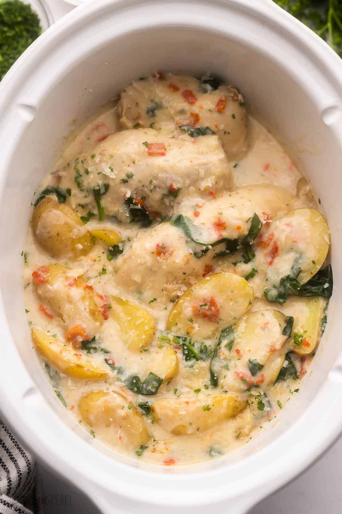 cooked italian chicken and potatoes in white crockpot with parsley beside.
