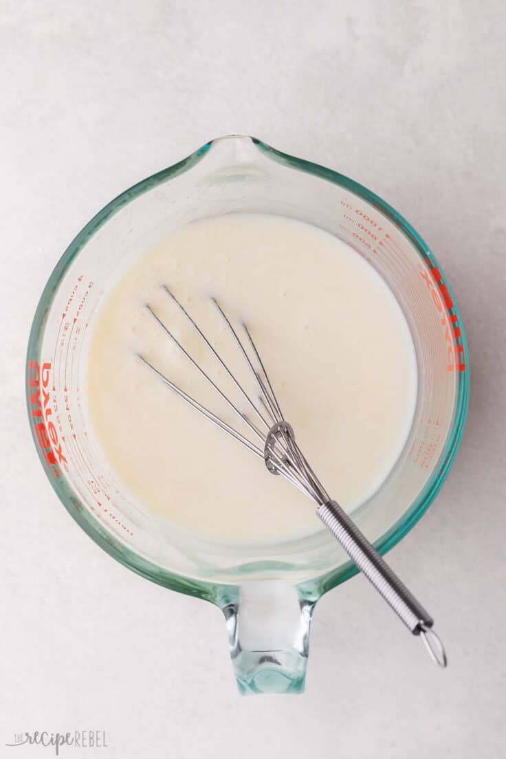 glass measuring cup with cream and a whisk.
