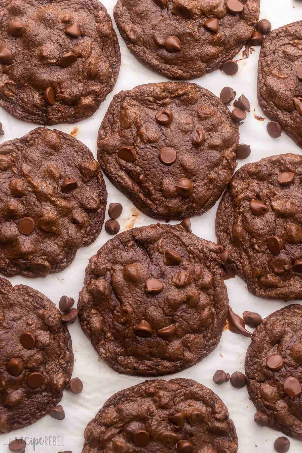 double chocolate chip cookies on parchment with chocolate chips around them.