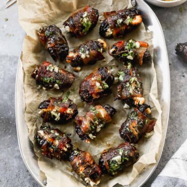 dates with bacon wrapped around them sprinkled with a green garnish
