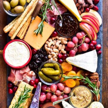 picture of cheese, meat, fruit, nuts, pickles, and olives on a tray