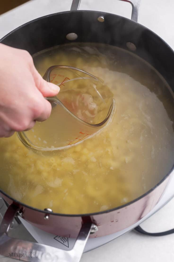 a measuring cup scooping water out of pot of pasta.