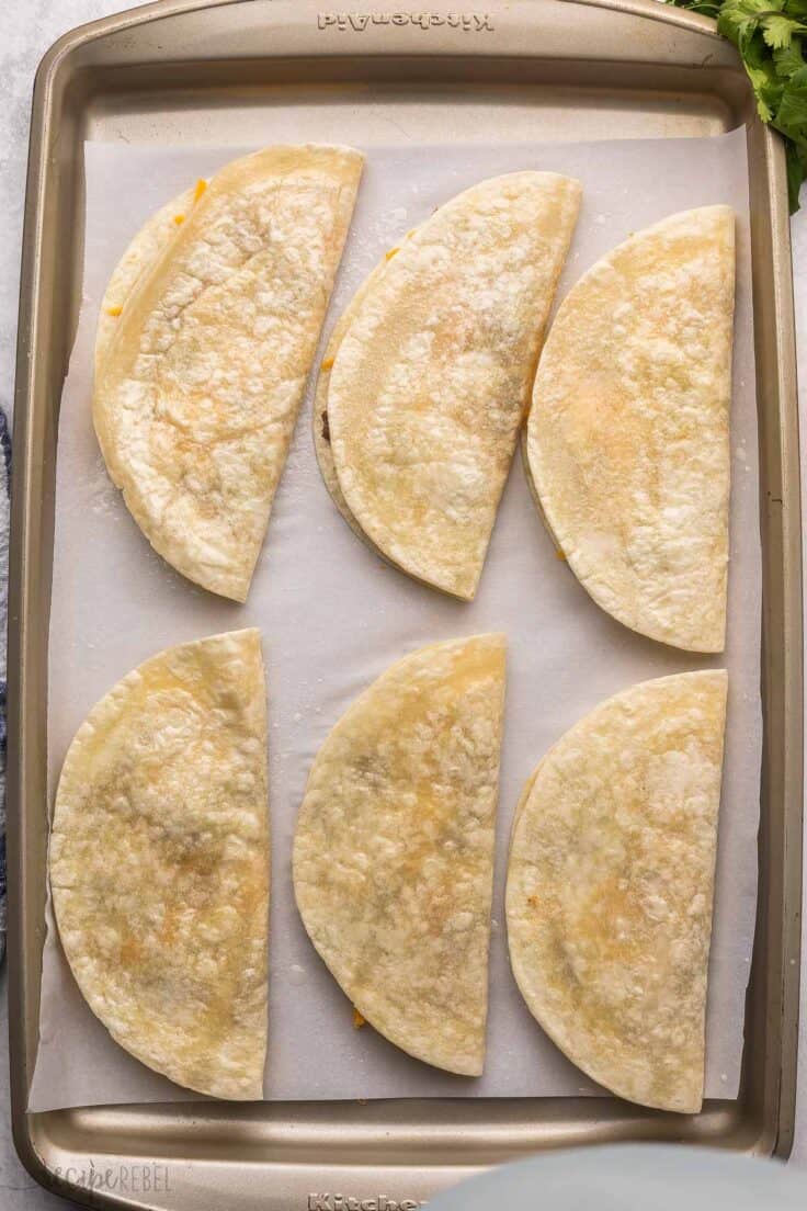 six unbaked tacos lying in a parchment lined pan.