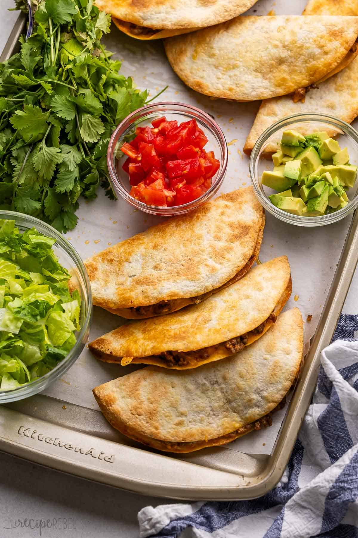 crispy baked tacos on a pan with lettuce and other toppings beside.