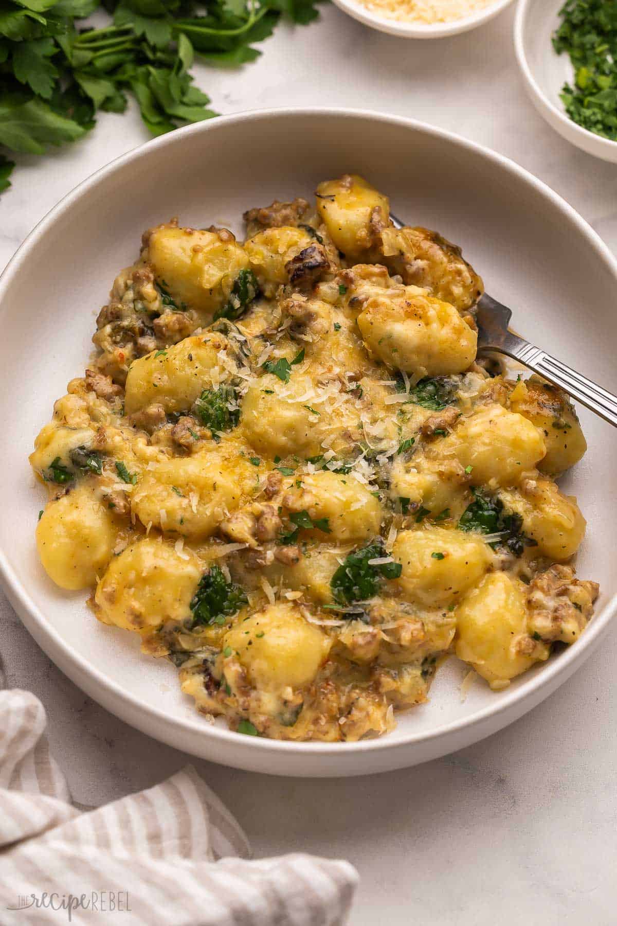 a fork in a plate of baked gnocchi topped with shredded parmesan.