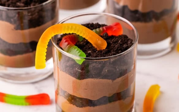 a glass cup of dirt cake with gummy works on top.