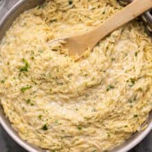 wooden ladle in a pan of garlic parmesan orzo.