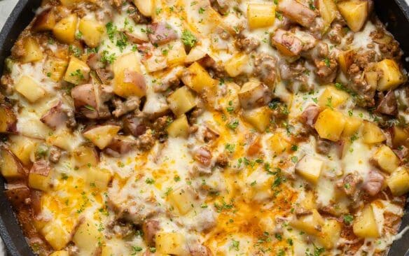 large pan of ground beef and potatoes topped with chopped parsley.