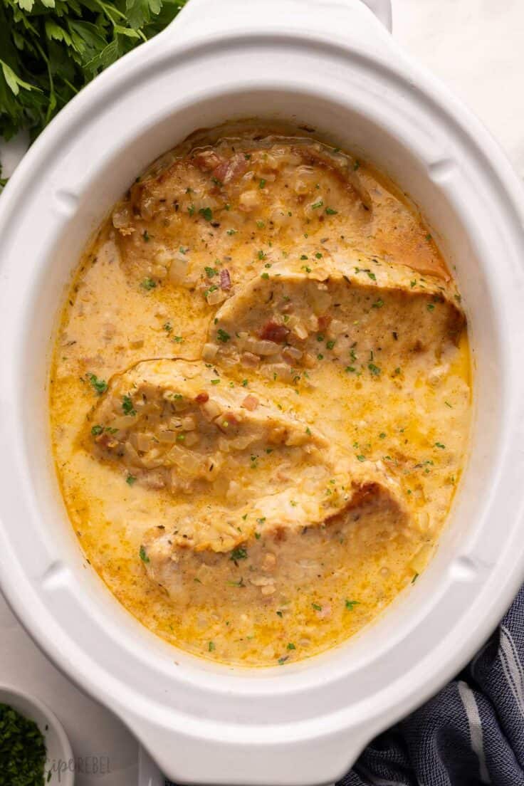white slow cooker filled with cooked pork chops and sauce.