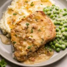 a pork chop on a plate with mashed potatoes and peas.