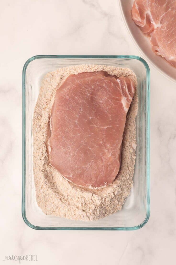 a pork chop in a glass bowl of flour mixture.