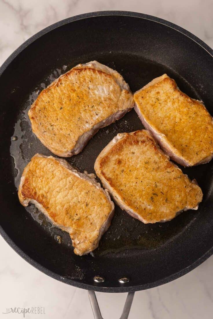 four seared pork chops in black frying pan.