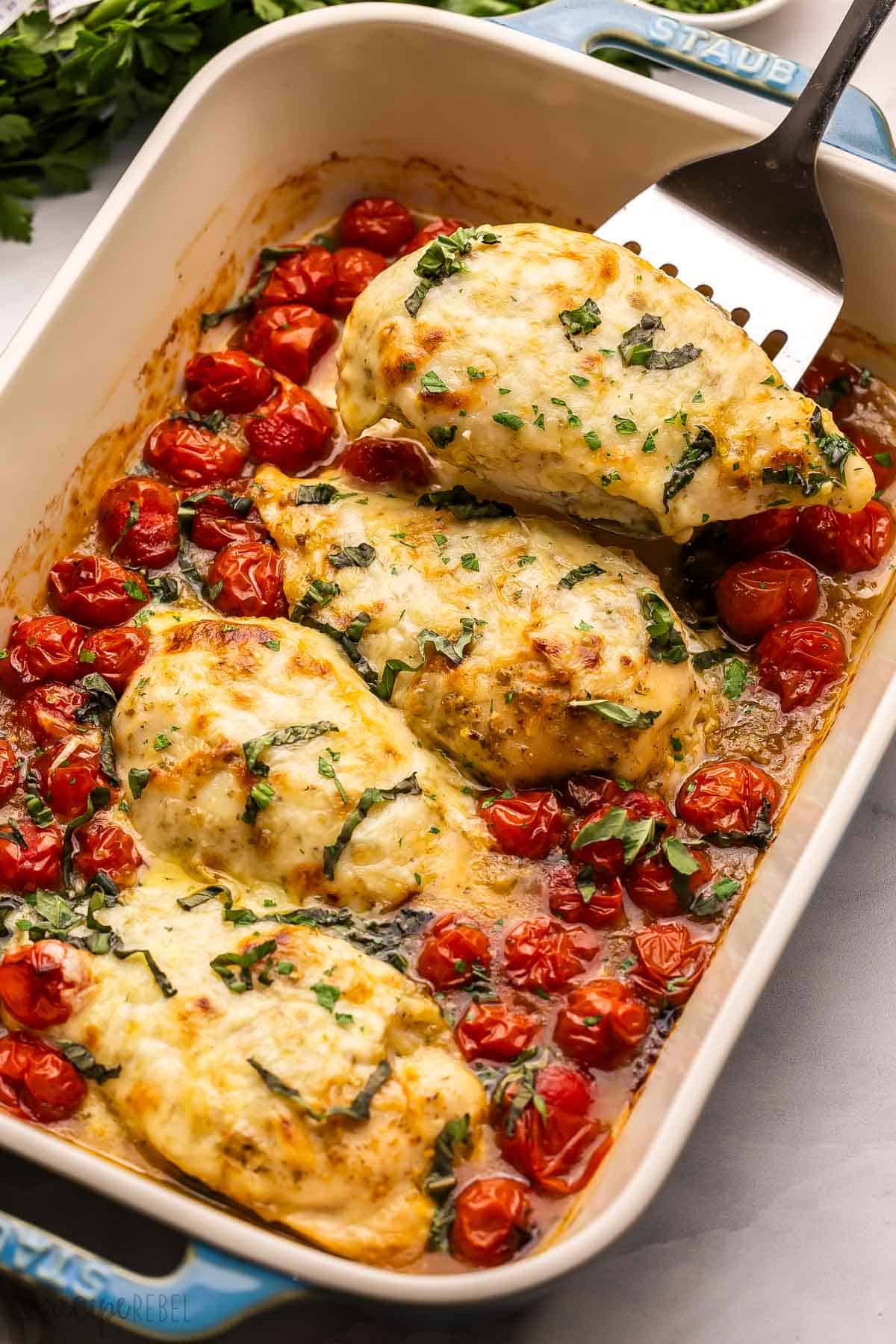 a baked caprese chicken breast being scooped out of pan.