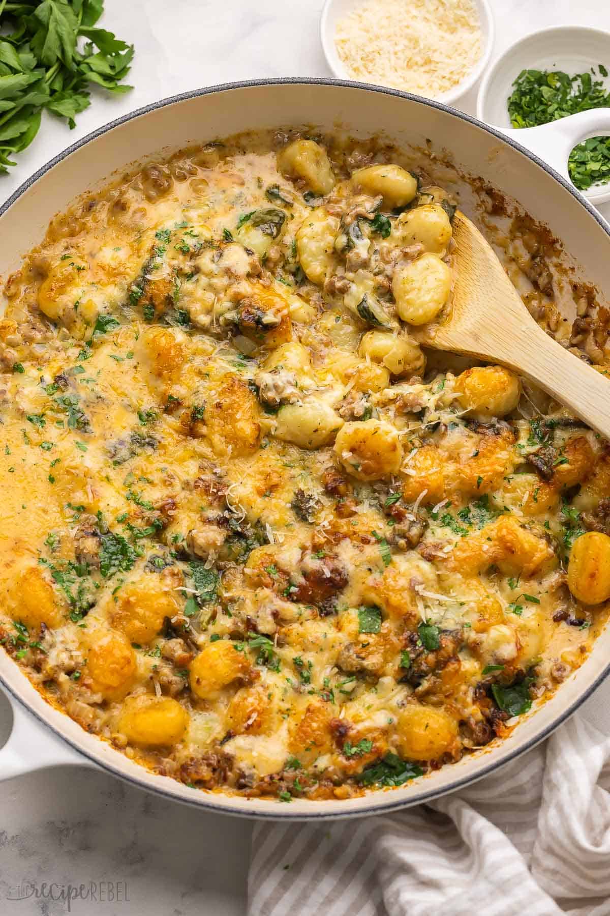 This Baked Gnocchi with Sausage is a quick and easy one-pot meal. It has a creamy sauce made with pillowy gnocchi, sautéed onions, Italian sausage, garlic, and spinach, baked until tender and bubbly. #dinner #recipe #gnocchi | easy dinner ideas | dinner recipes | gnocchi recipes | italian sausage recipe | one pan meals large skillet full of baked gnocchi with sausage.