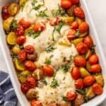 white baking dish full of caprese chicken and potatoes topped with chopped basil.