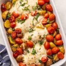 white baking dish full of caprese chicken and potatoes topped with chopped basil.