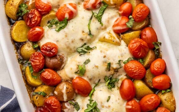 white baking dish full of caprese chicken and potatoes topped with chopped basil.