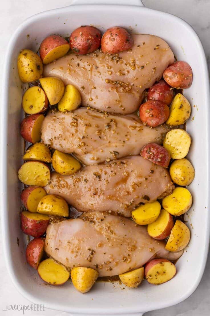 chicken breasts and potatoes in a white baking dish.