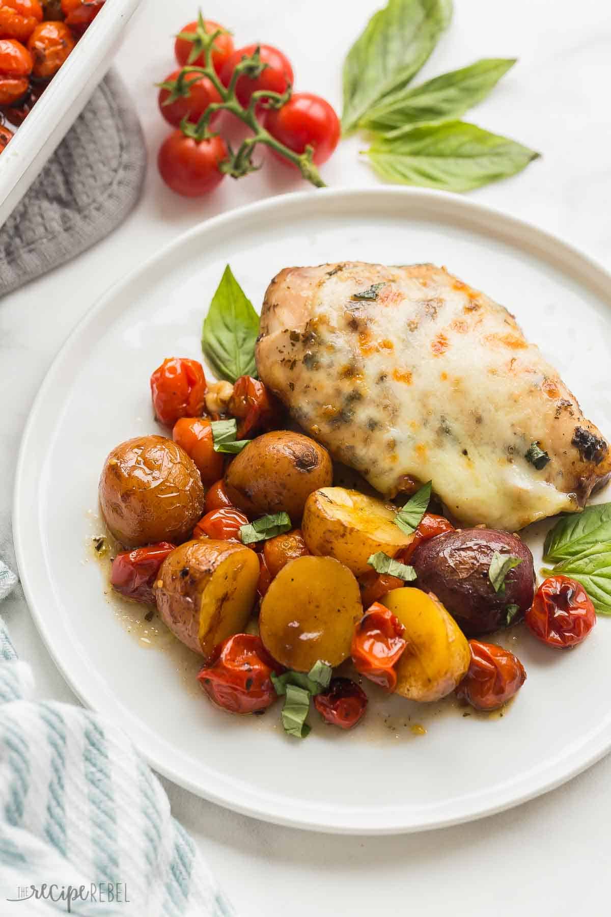 white plate with caprese chicken and potatoes with basil behind it.