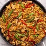 chicken chow mein in a black frying pan.