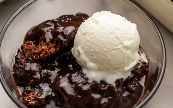 a glass bowl filled with hot fudge sundae cake and a scoop of vanilla ice cream on top.
