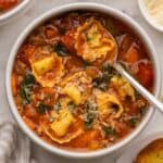 square image of sausage tortellini soup in bowl with spoon.