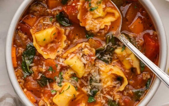 square image of sausage tortellini soup in bowl with spoon.