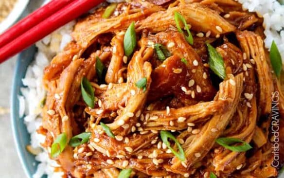 crockpot asian sesame chicken on a bed of white rice with red chopsticks on the side