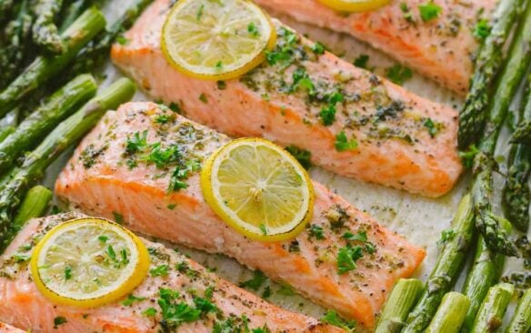 salmon fillets lined up on a baking sheet surrounded by asparagus