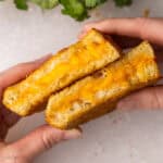 hands holding two halves of a grilled cheese sandwich.