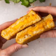 hands holding two halves of a grilled cheese sandwich.