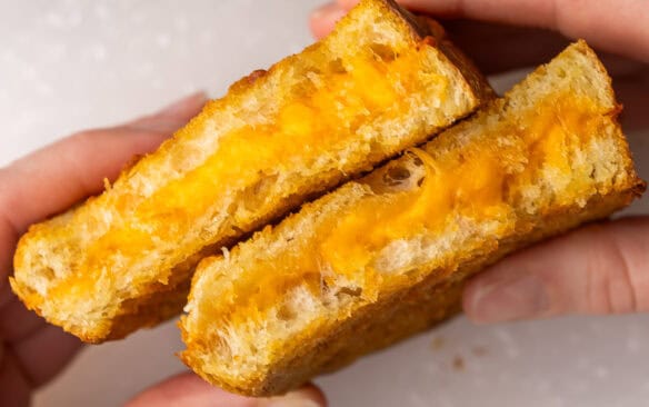 hands holding two halves of a grilled cheese sandwich.