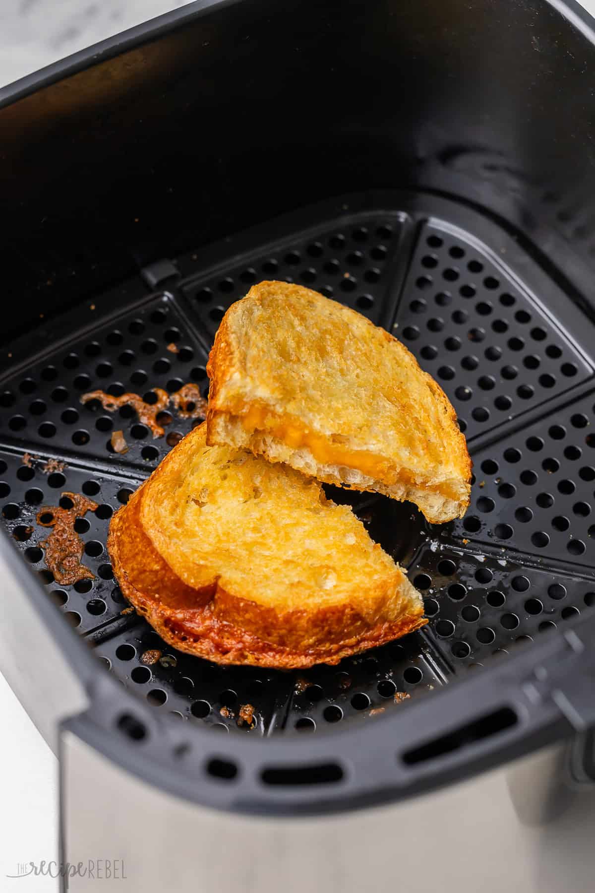 an air fryer basket with a halved grilled cheese sandwich in it.