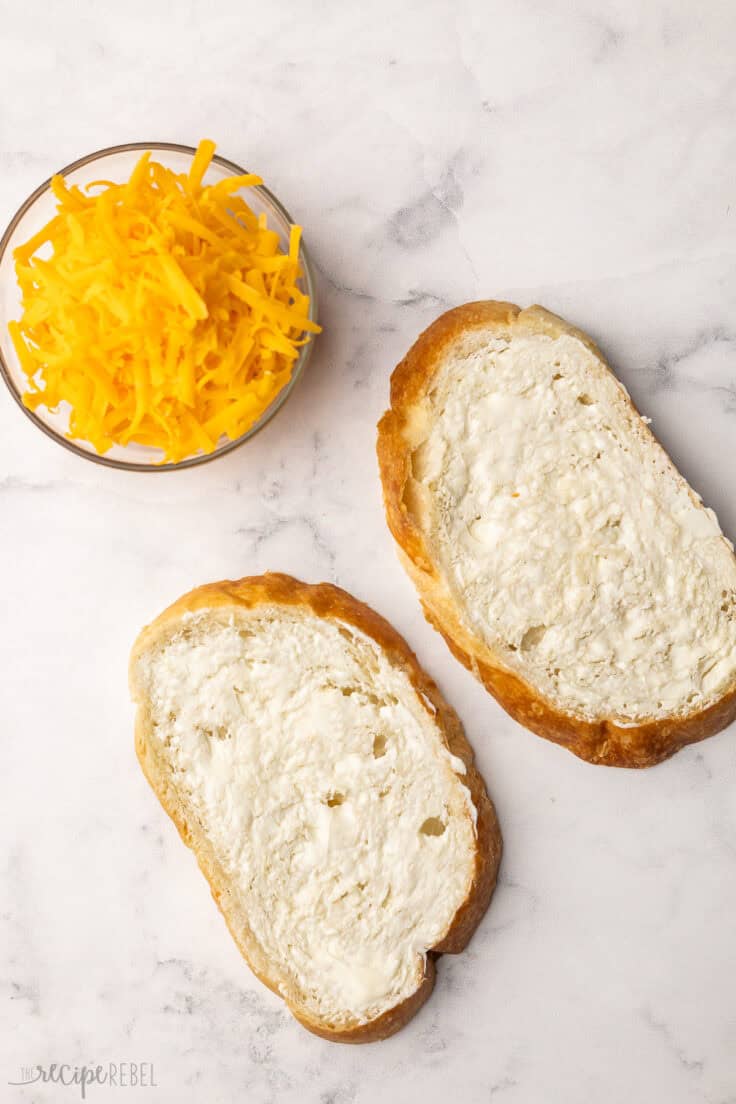 two pieces of buttered bread with a bowl of shredded cheddar.