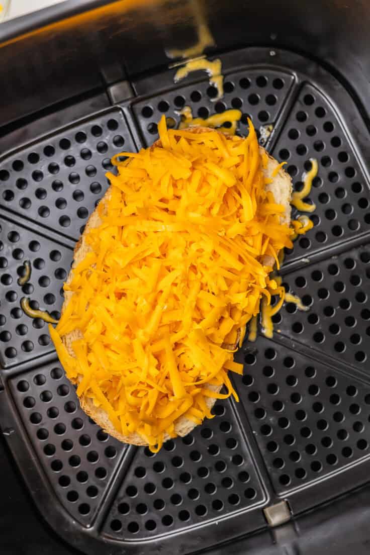 a piece of bread in an air fryer topped with shredded cheddar cheese.