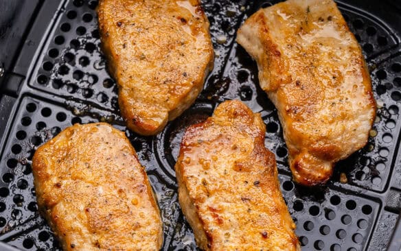 four air fryer pork chops in black air dryer basket.