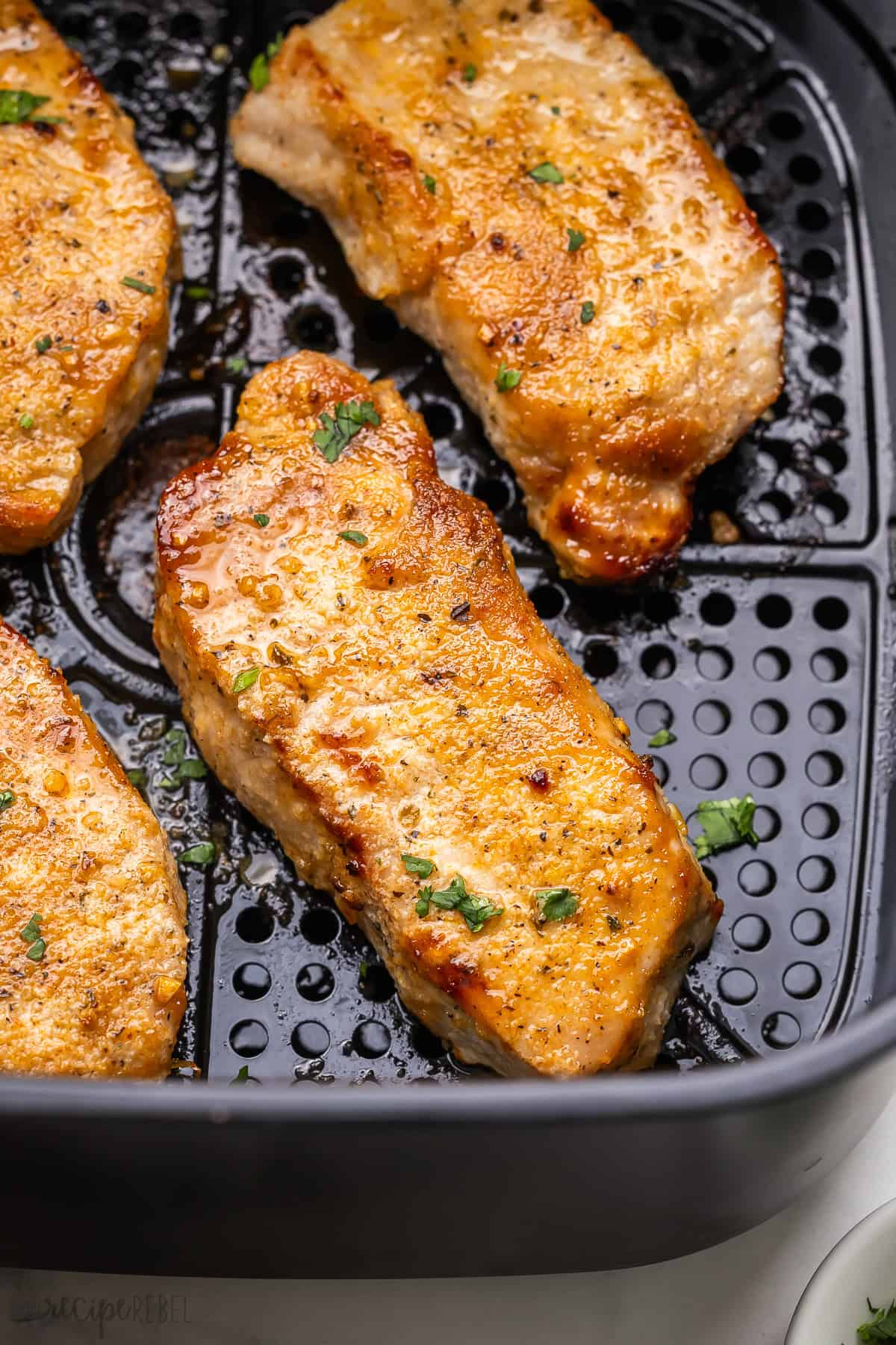 Make juicy Air Fryer Pork Chops with this simple recipe! A few simple ingredients like boneless pork chops, oil, and my homemade spicy rub create super juicy chops that are perfect for pairing with your favorite sides. #airfryer #recipe #dinner | air fryer recipes | air fryer pork | dinner recipes | easy dinner ideas | boneless pork chops | easy air fryer recipe air fryer pork chop in a black air fryer topped with chopped parsley.