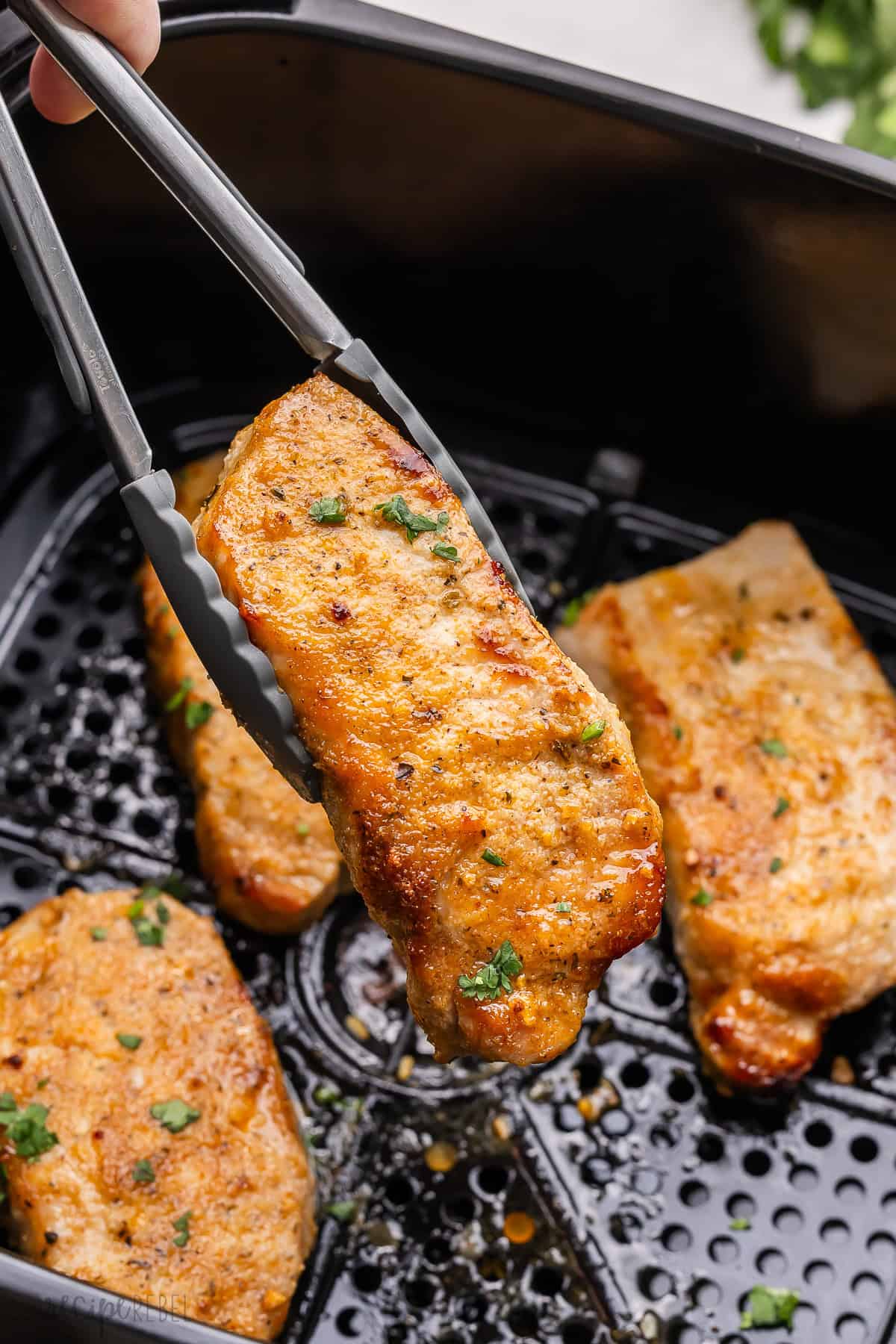 tongs lifting a pork chop out of an air fryer basket.