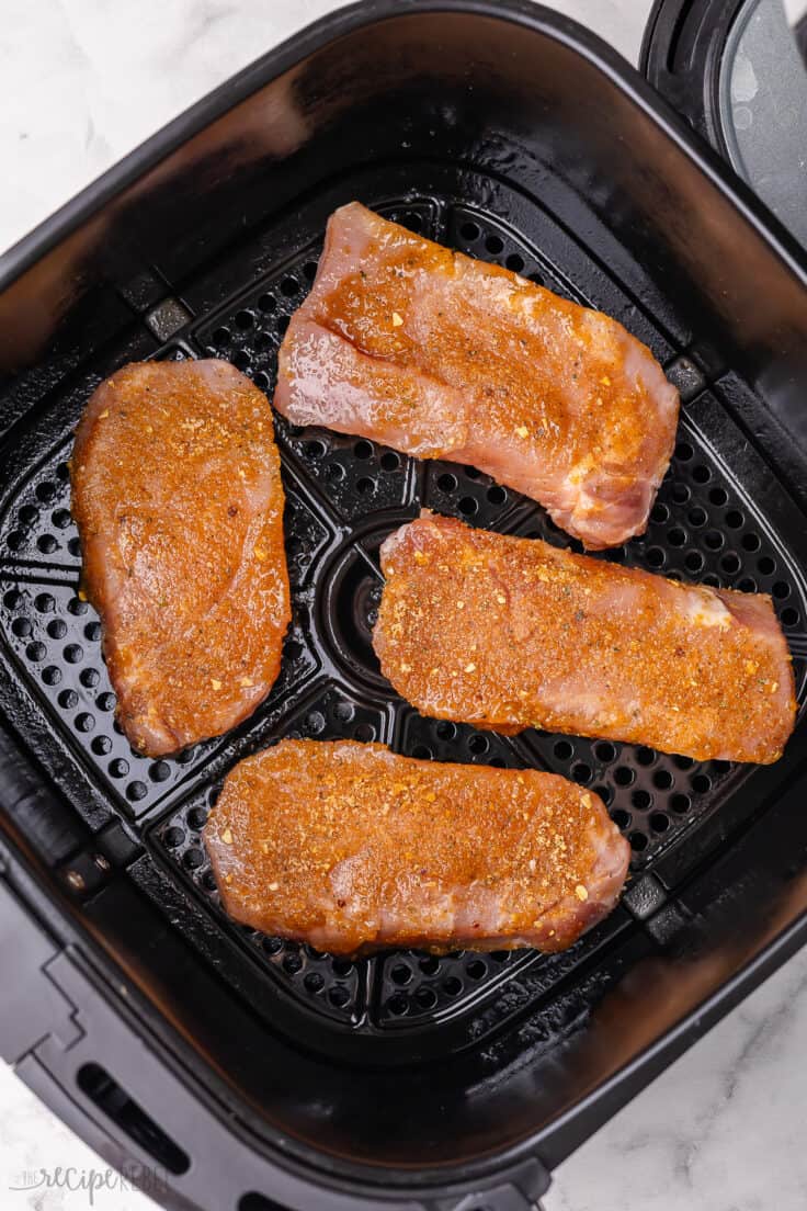four uncooked pork chops in air fryer basket.
