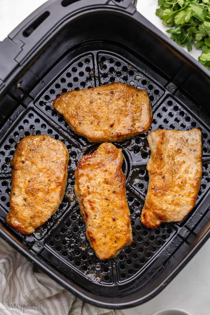 four cooked air fryer pork chops in air fryer basket.