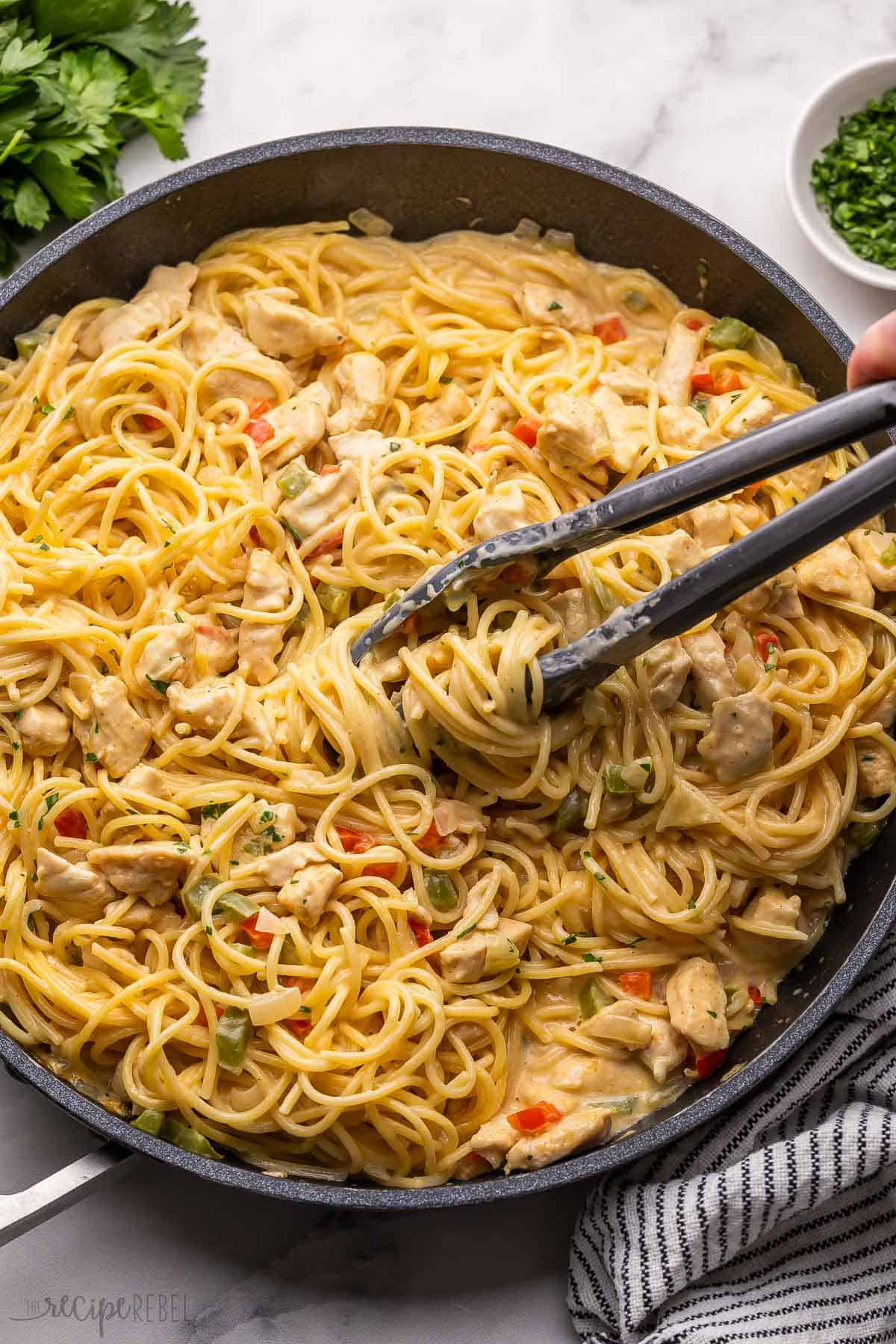 tongs serving chicken spaghetti out of a black pan.