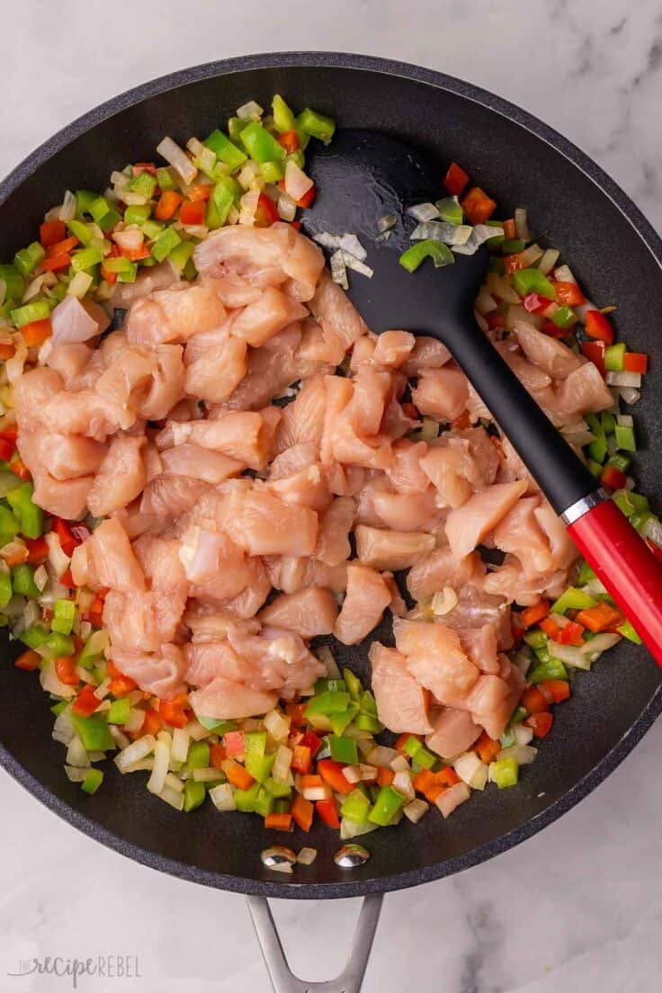 uncooked chicken added into black pan with other ingredients.