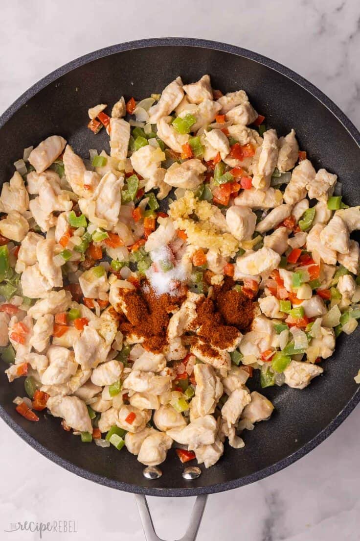 spices added to black pan with chicken and peppers.
