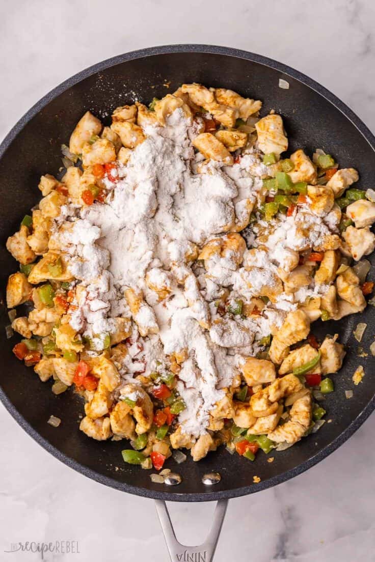 flour added to ingredients in black pan.
