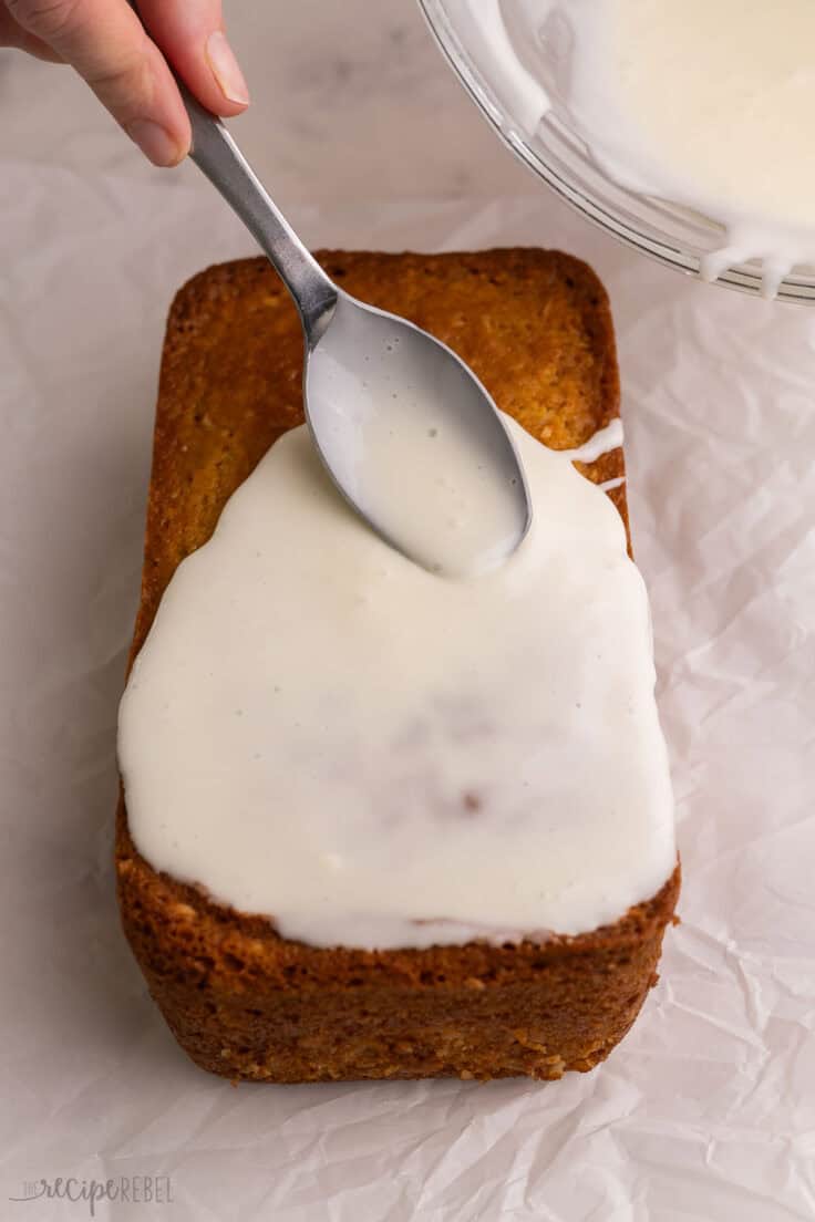 a spoon spreading glaze over the loaf of coconut bread.