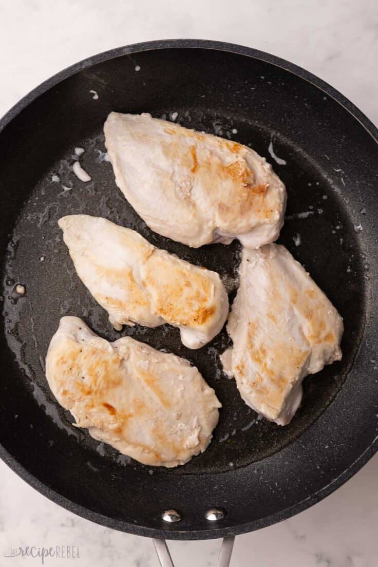 four chicken breast browning in a frying pan.