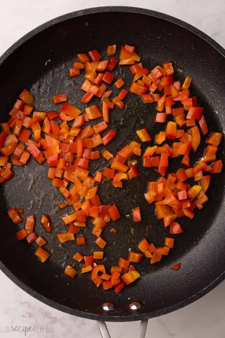 chopped red peppers sauteing in a black frying pan.