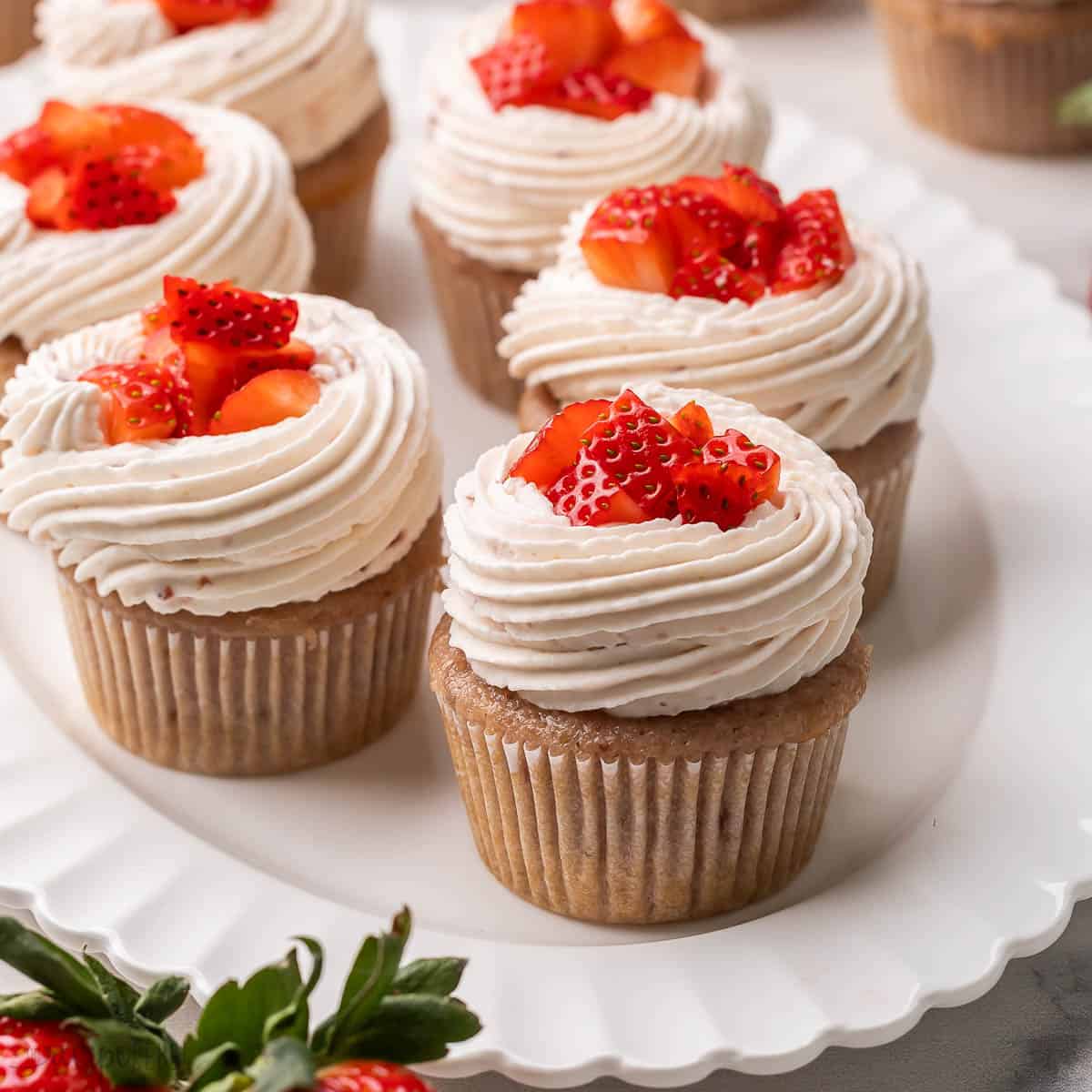 strawberry cupcakes topped with chopped strawberries on a white plate.