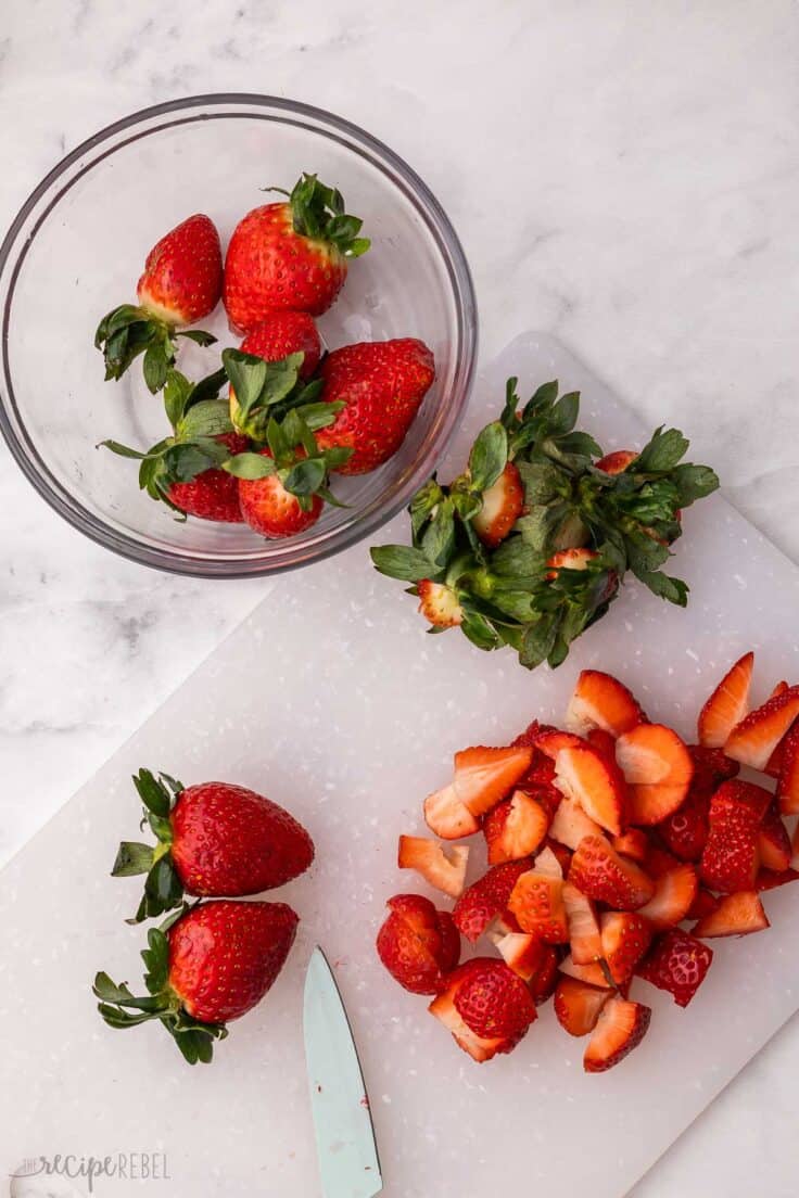 white cutting board with sliced strawberries and knife.