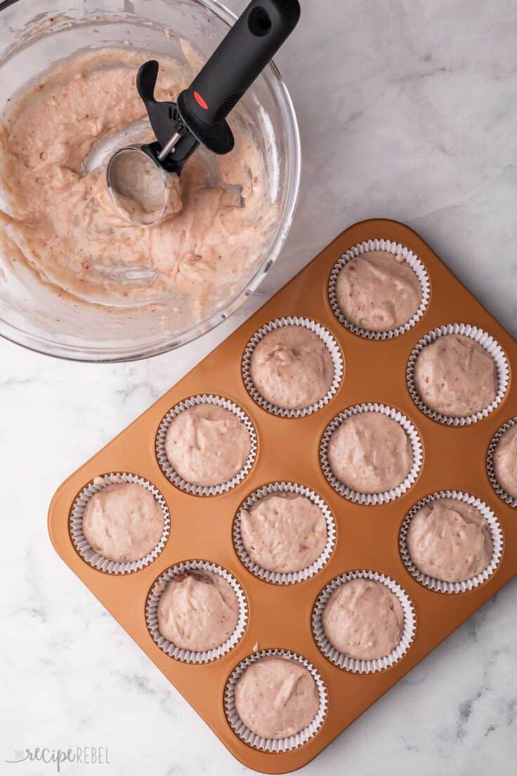 cupcake pan filled with liners and batter with mixing bowl beside.